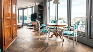 A spacious room with a large wooden wardrobe, a round dining table with chairs, a television, and a view of the city through large windows. - Hirschen Oberkirch  (Oberkirch)