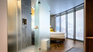 A modern hotel room with a glass shower enclosure, a bed with a white mattress, and a view of the city through large windows. - Hirschen Oberkirch  (Oberkirch)