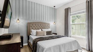 Un dormitorio con una cama grande, un televisor sobre un mueble bajo y una ventana con cortinas.