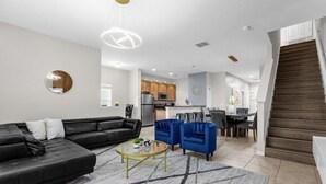 Una sala moderna con un sofá negro, sillas azules, una mesa de centro y una escalera que lleva a una zona de cocina.
