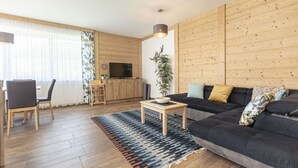 Una sala de estar moderna con un sofá oscuro, piso de madera, un televisor y un comedor con sillas y una mesa.