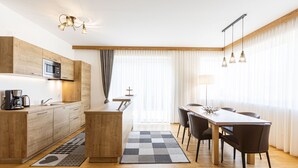 Une cuisine moderne avec des meubles en bois, un four à micro-ondes et une machine à café. On y trouve un coin repas avec une table et des chaises, ainsi qu’une grande fenêtre avec des rideaux.