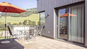Une terrasse extérieure avec une table et des chaises, un parasol rouge et une vue sur un paysage verdoyant.