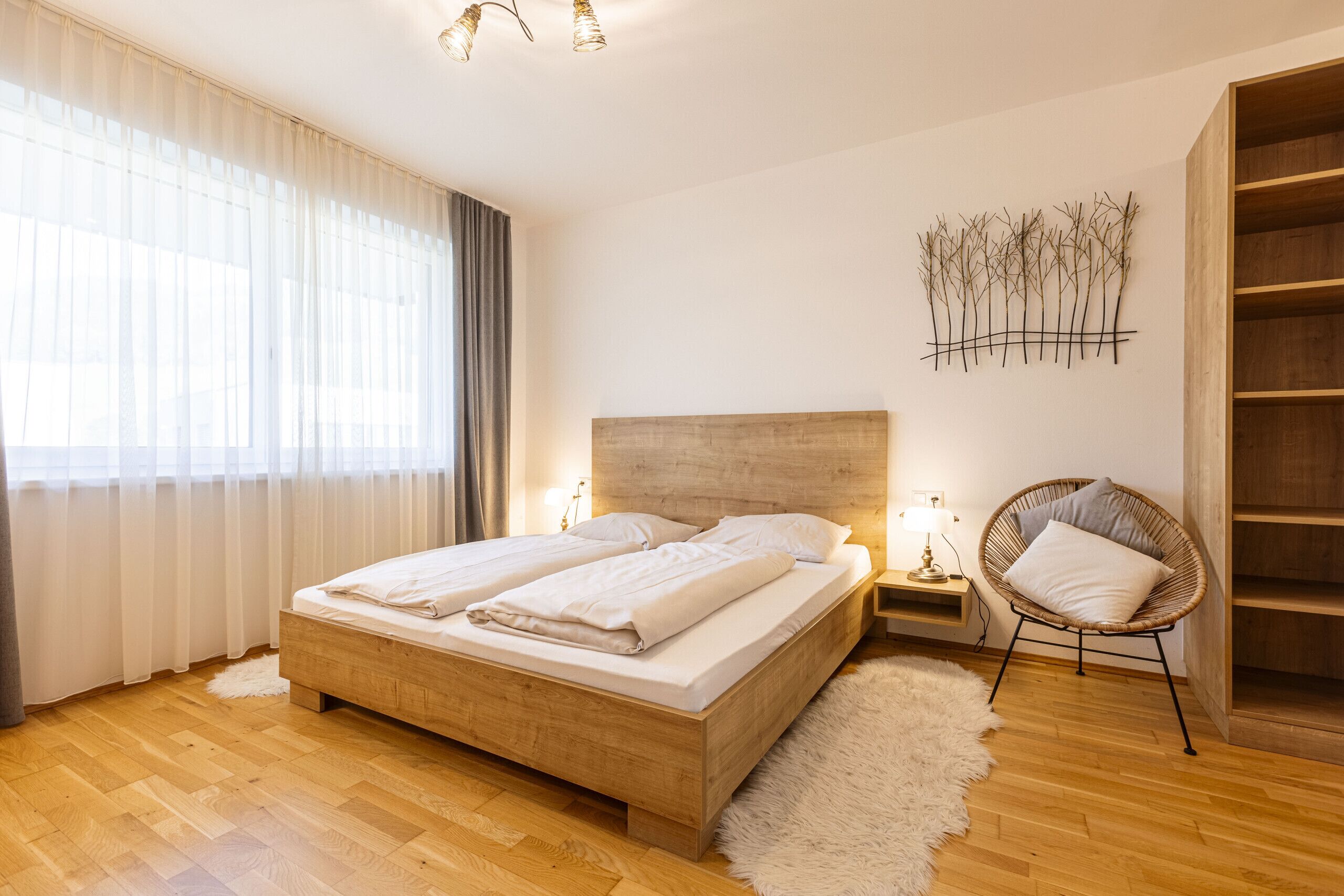 Um quarto com uma cama de madeira, um tapete felpudo branco, uma cadeira de vime e uma decoração de planta fixada na parede.