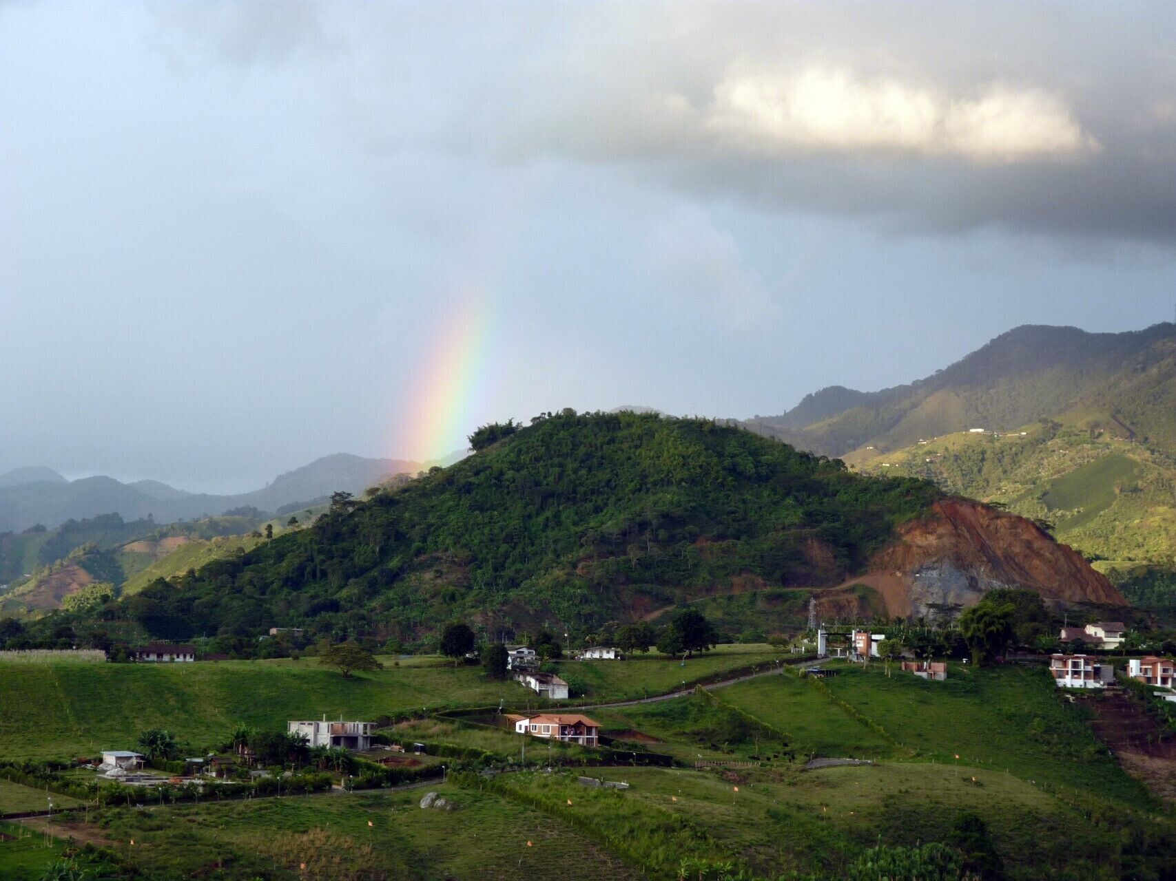 A rural landscape with a hill, houses, and a rainbow.