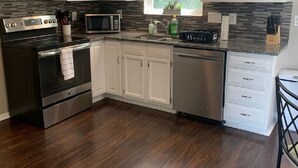 Una cocina moderna con armarios blancos, una estufa de acero inoxidable, un microondas y un lavavajillas.