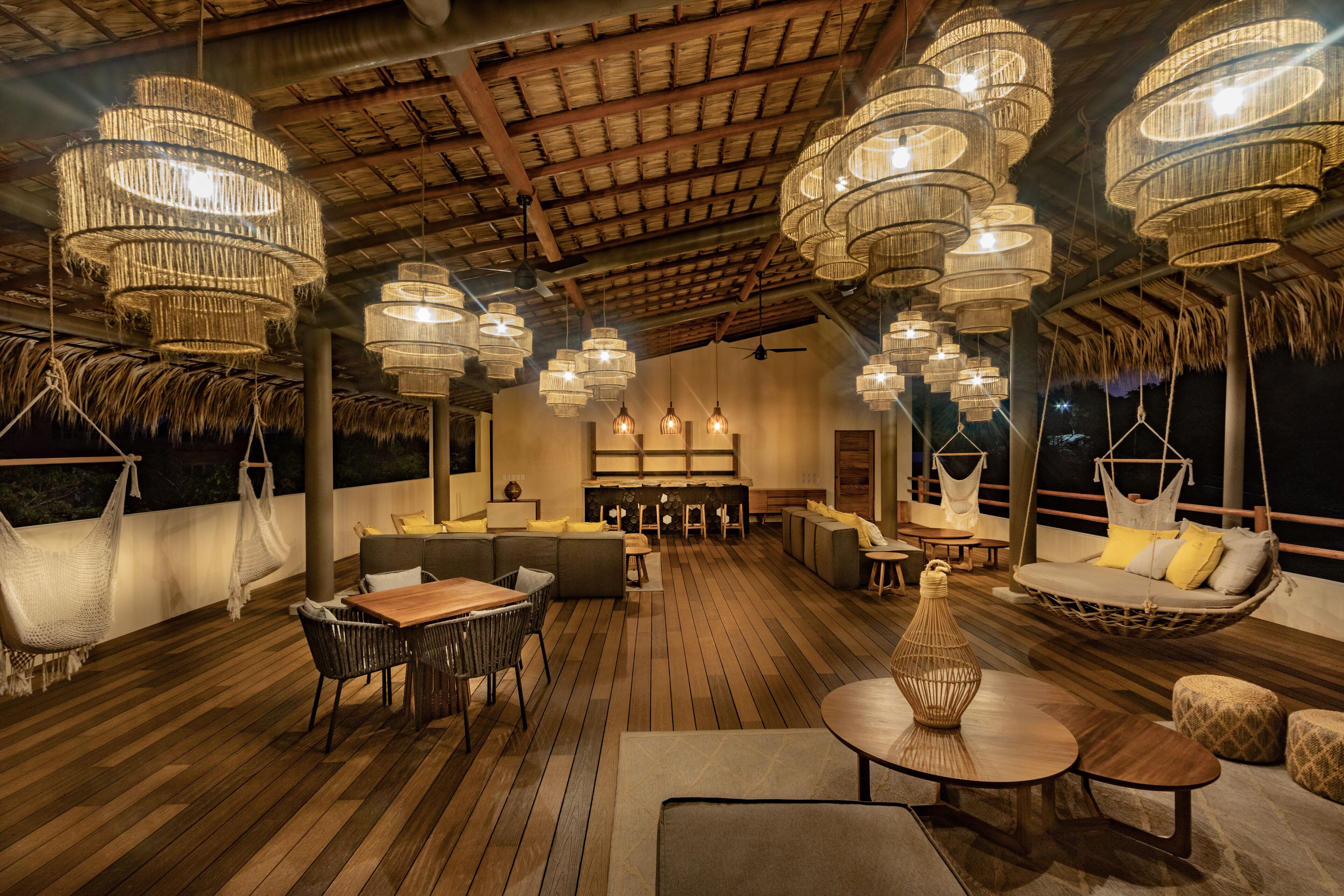 Une terrasse en bois agrémentée de lustres en osier suspendus, de sièges confortables et d’un coin bar.