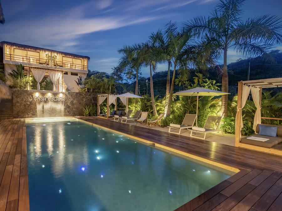 A pool area with a wooden deck, lounge chairs, and a waterfall feature.