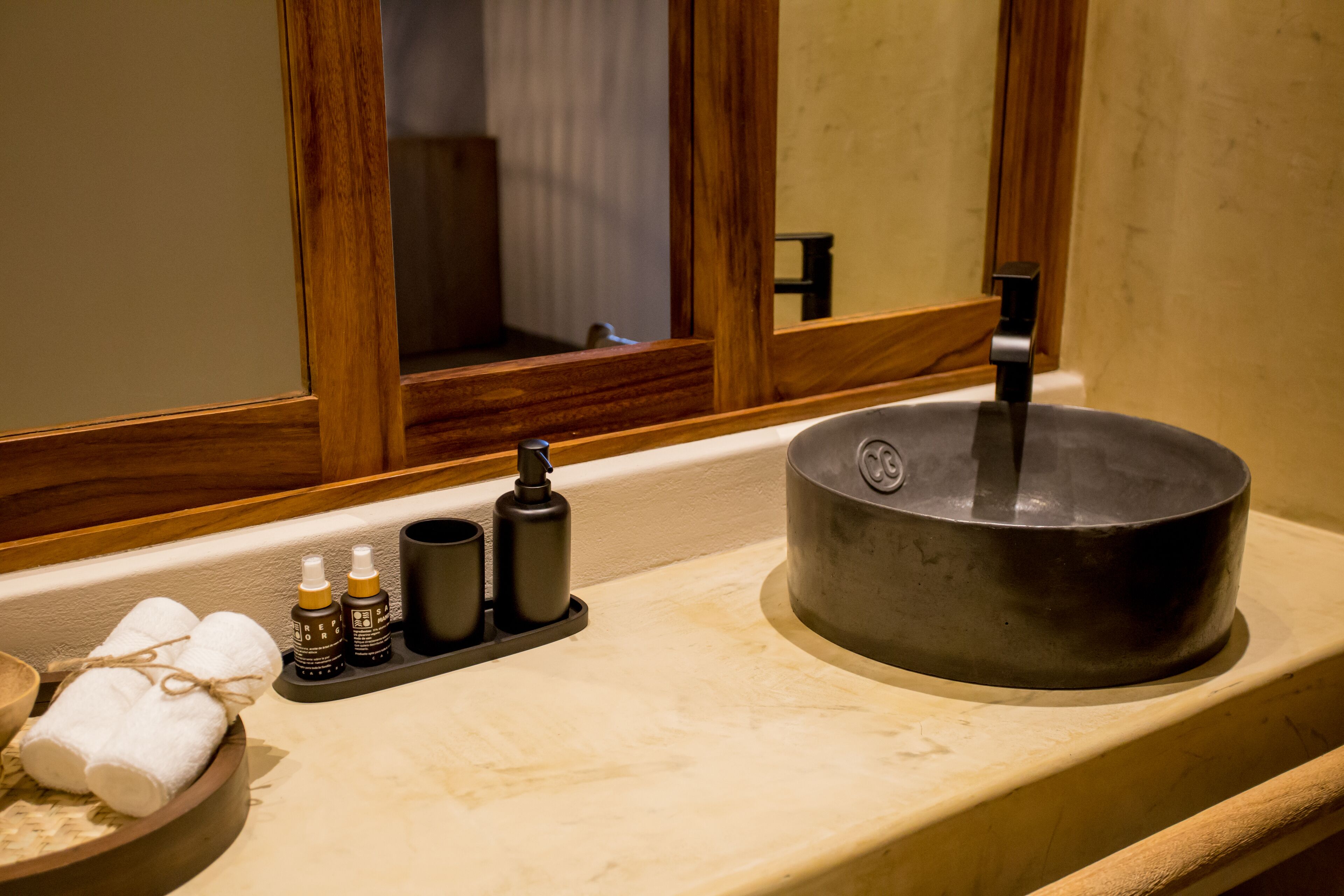 A bathroom with a wooden-framed mirror, a sink with a black basin, and toiletries on the countertop.