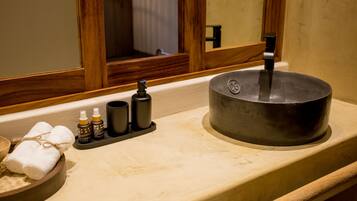 A bathroom with a wooden-framed mirror, a sink with a black basin, and toiletries on the countertop.
