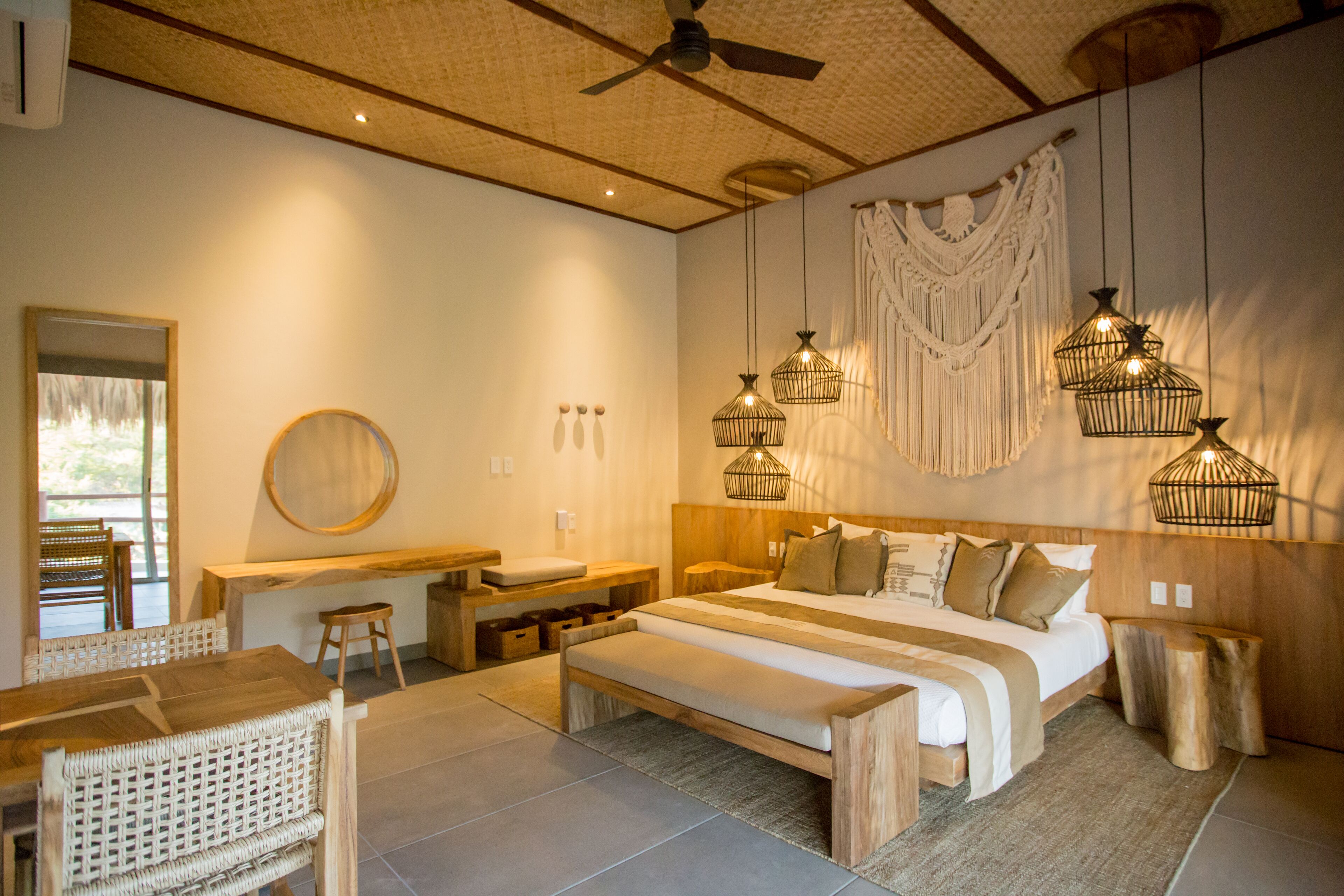 A spacious bedroom with a large bed, wooden furniture, and macramé wall decor.