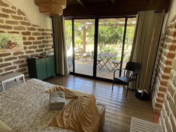 Una habitación con una cama, un armario verde, una silla y una mesa frente a una puerta corrediza de vidrio.