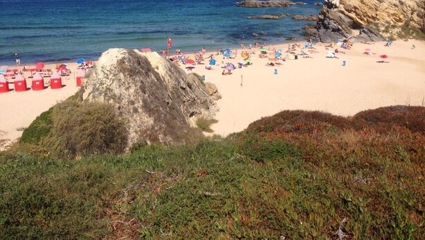 Une plage avec des parasols rouges et un promontoire rocheux.