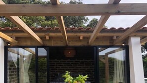 Une terrasse en bois avec une table et des chaises, un mur en briques et une structure en forme de pergola.