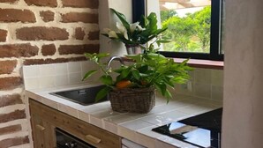 Une cuisine avec un mur en briques, des carreaux blancs, un évier, un lave-vaisselle et une fenêtre donnant sur un espace verdoyant.