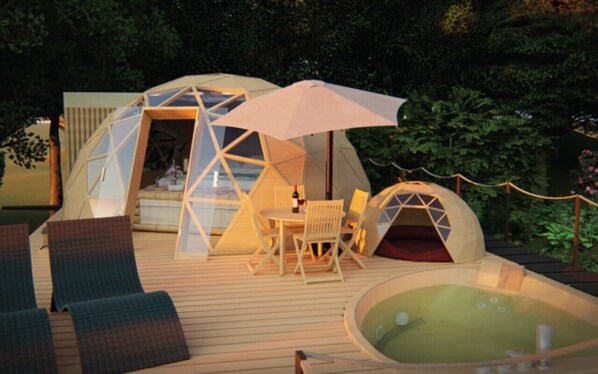 Ein kuppelförmiges Zelt mit Tisch und Stühlen, einem Whirlpool und einer Holzterrasse.