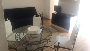 En stue med et glasbord, en sort sofa og et fjernsyn på et sort skab.