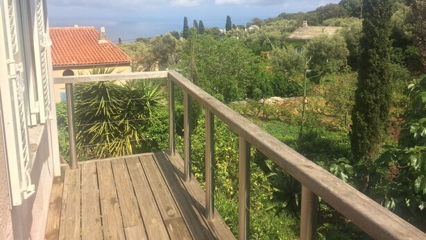En træterrasse med gelænder i metal, med udsigt over en have med forskellige planter og træer.