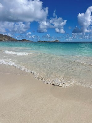 A beach with clear turquoise water, gentle waves, and distant hills.
