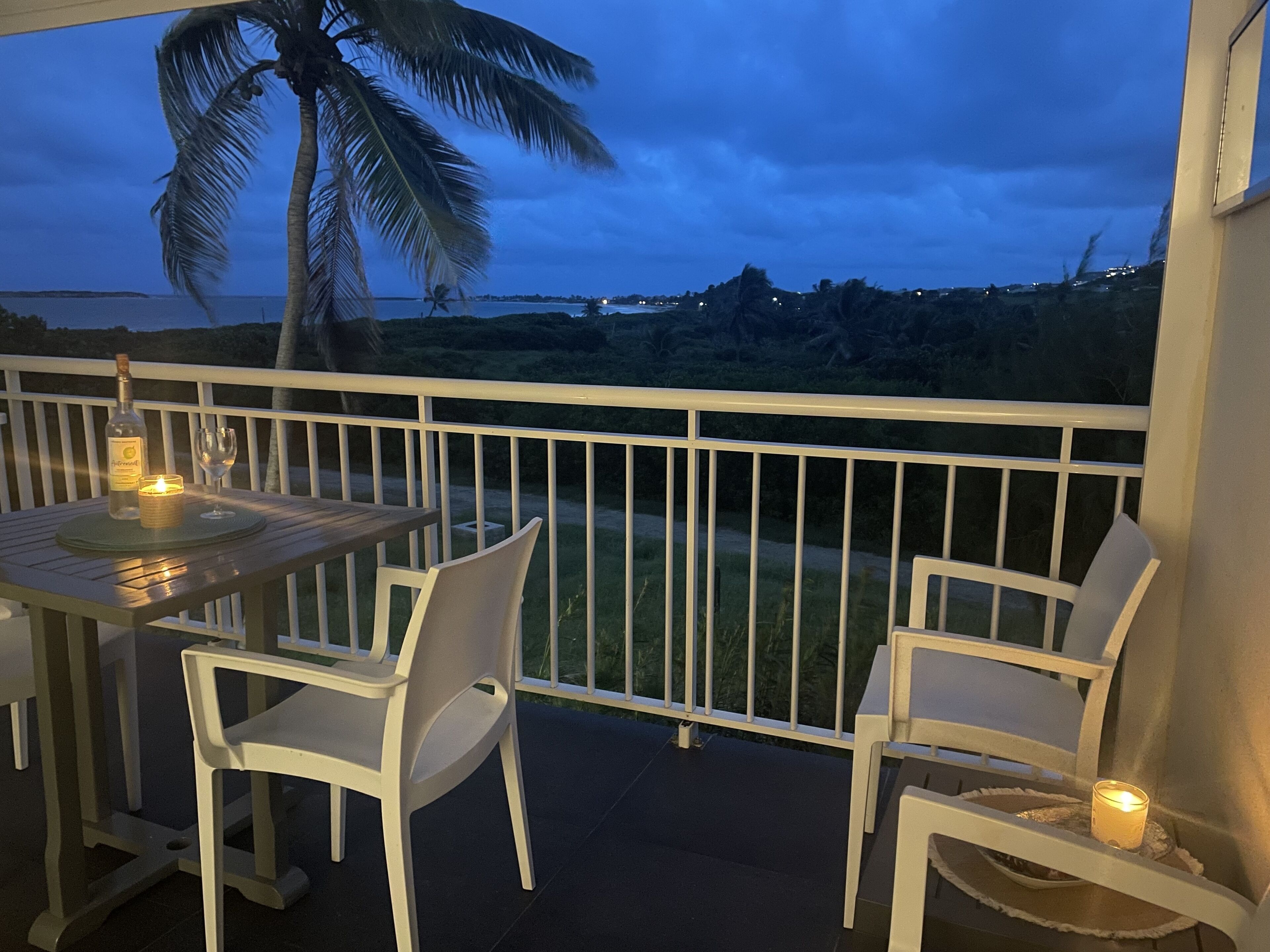 Un balcon avec une table et des chaises, une bougie, et une vue sur l’océan et les palmiers.