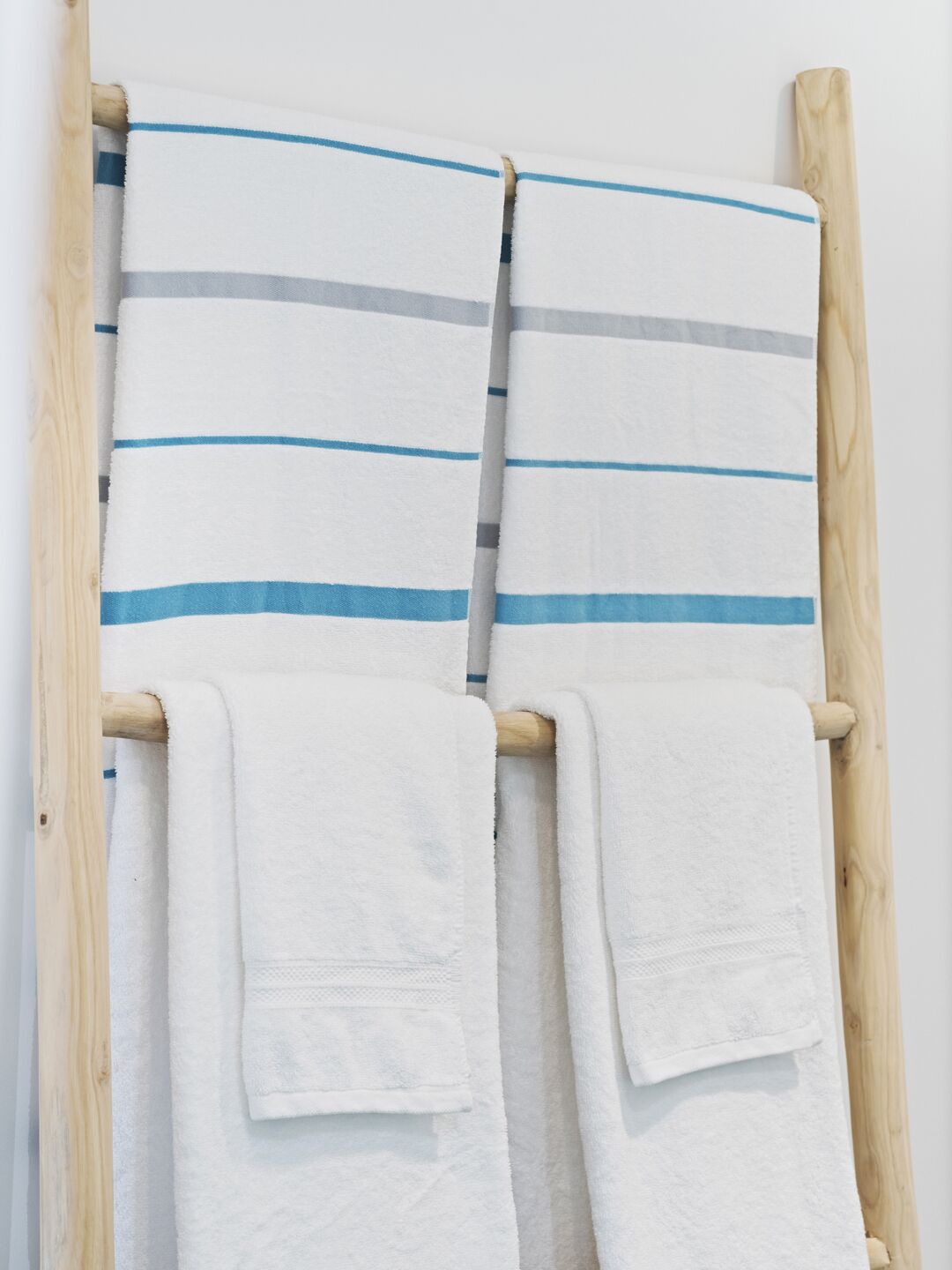 Een houten handdoekhouder met vier witte handdoeken, elk met blauwe strepen.