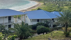 A coastal hotel with blue roofs, a beach view, and lush greenery. - Beachfront Orient Bay 1‑BR Condo • Mont Vernon • Balcony • Pool • Fast Wi‑Fi (Cul de Sac)