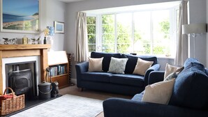 A cozy living room with a fireplace, a blue sofa, and a large window with curtains. - Apple Blossom - Chideock, Bridport (Chideock)