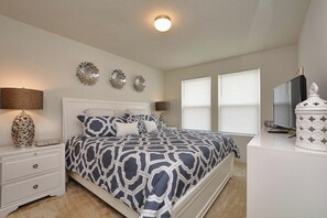 A bedroom with a bed, nightstands, a lamp, wall decor, and a television.