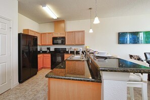 A kitchen with wooden cabinets, a black refrigerator, a microwave, and a granite countertop. - Lakefront Disney Retreat | Pet-Friendly | Family Fun in Compass Bay (Kissimmee)