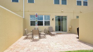 A building with a patio area featuring a table and chairs, a flagpole, and a sliding glass door.
