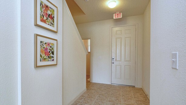A hallway with two framed floral artworks on the wall, a white door at the end, and a tiled floor.