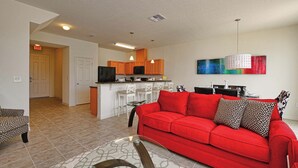 A modern living room with a red sofa, a glass coffee table, and a kitchen in the background.