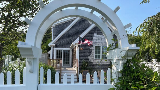 Une maison avec une clôture blanche en bois, un porche et un drapeau américain.
