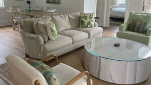 Un salon spacieux avec un canapé beige, une table basse en verre et un fauteuil en bois.