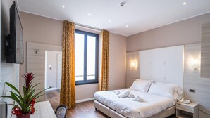 Ein modernes Hotelzimmer mit einem großen Bett, Nachttischen, einem Schreibtisch und einer Zimmerpflanze.