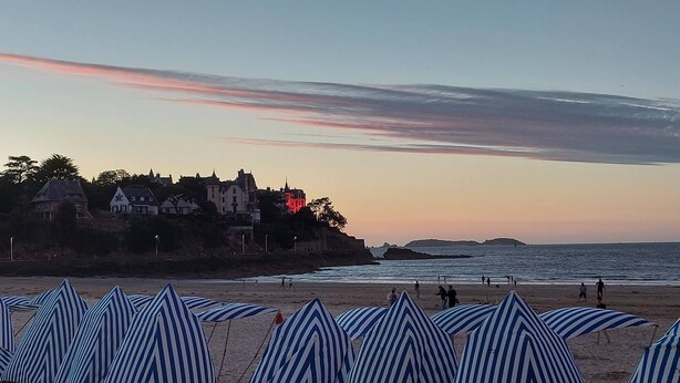 A beach with striped beach umbrellas and a row of houses in the background.
