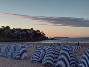 Una playa con sombrillas de rayas y una hilera de casas al fondo.