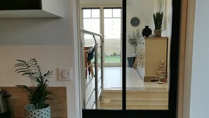 A modern kitchen with a wooden countertop, a potted plant, and a sliding door leading to a living area with a staircase, a clock, and a small Christmas tree.