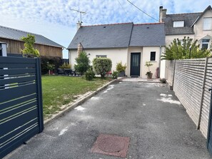 A residential property with a paved driveway, a black metal gate, and a small garden with potted plants.