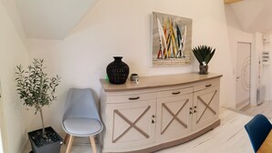 A modern living room with a sofa, a dining table, and a kitchen area with cabinets and a plant.