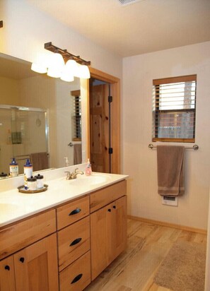 A bathroom with a wooden vanity, a large mirror, and a window with blinds. - Magical Cabin in Pinetop Lakes (Pinetop)
