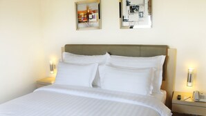 A neatly made bed with white linens, a wooden headboard, and two bedside lamps.