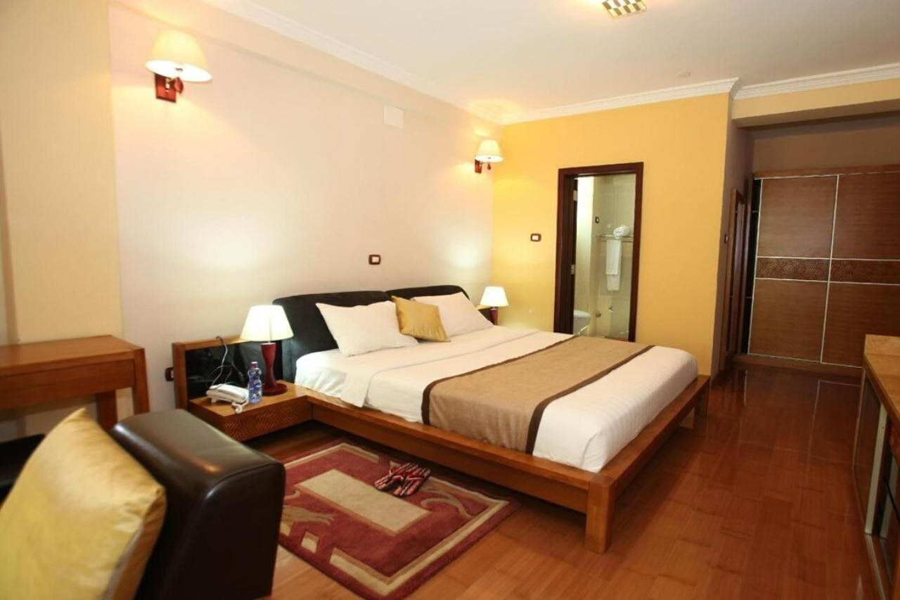 A hotel room with a wooden bed, two bedside lamps, a nightstand, a chair, and a red rug.