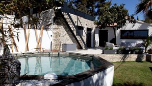 Ein moderner Poolbereich mit einer Steinwand, einer Lounge mit Sitzgelegenheiten im Freien und einer Treppe, die zu einer erhöhten Ebene führt.