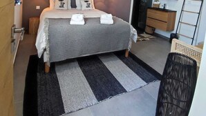 Ein modernes Schlafzimmer mit einem großen Bett, zwei Nachttischlampen, einem Kunstwerk aus Holz über dem Bett und Blick ins Badezimmer.
