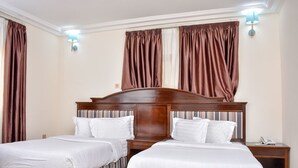 A hotel room with two beds, a wooden headboard, a nightstand with a phone, and brown curtains. - Sonia Hotel (Accra)