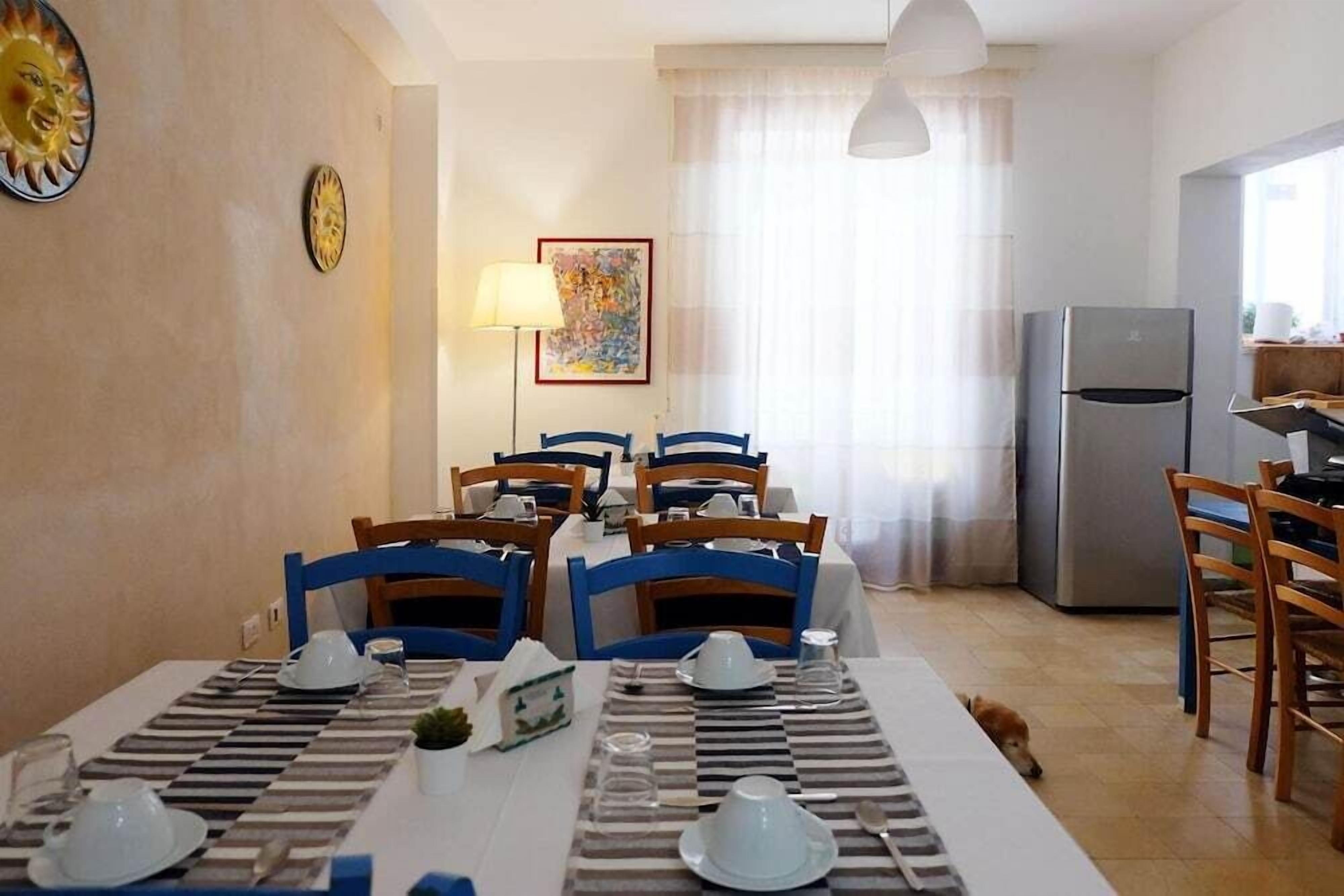 A dining area with a table set for four, blue chairs, a refrigerator, and a lamp.