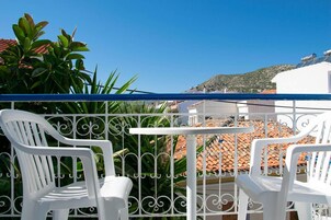 A balcony with white plastic chairs and a table, overlooking a terracotta-tiled building and a hillside.