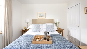 Une chambre d’hôtel avec un lit, une table de chevet avec une lampe, un plateau avec des articles pour le petit-déjeuner et un tableau encadré au mur.