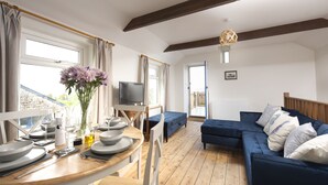 Un salon moderne avec un plancher en bois, un canapé bleu, une table à manger dressée avec des assiettes et des verres, et un téléviseur posé sur un meuble.